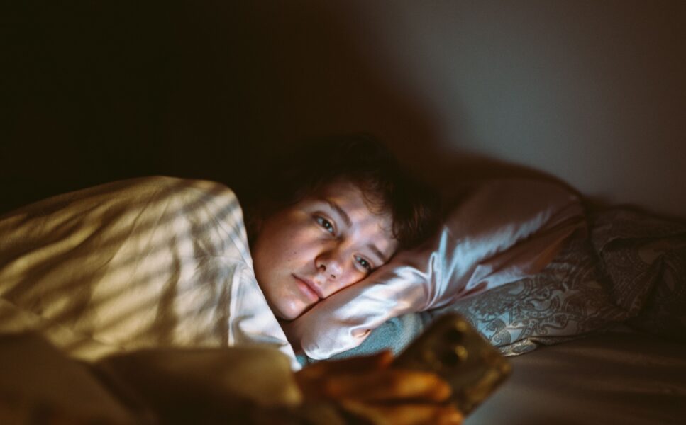 A woman lying in bed in a dark room, using her phone