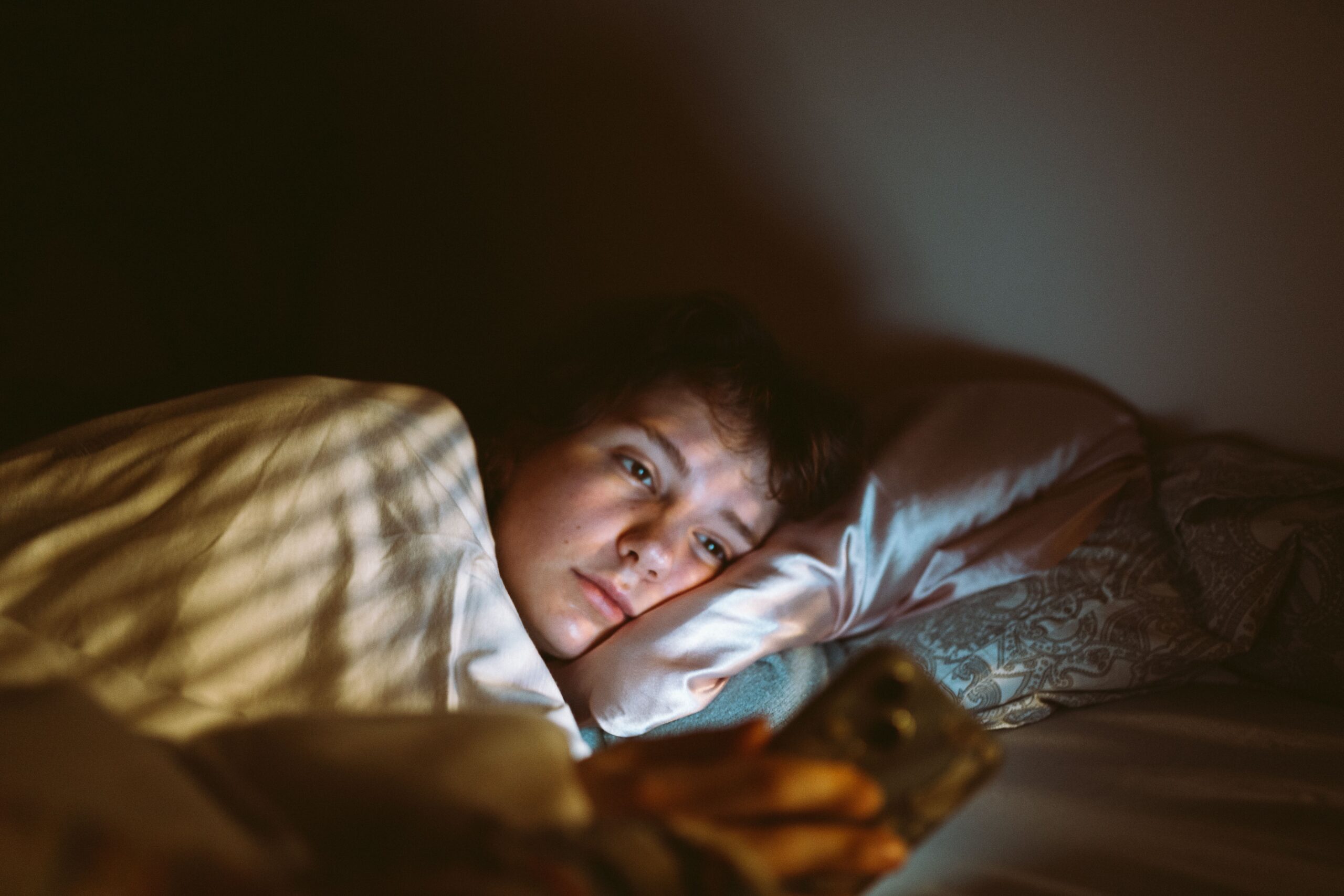 A woman lying in bed in a dark room, using her phone